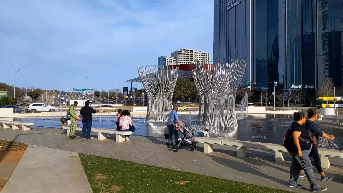 Children playing in fountain in urban park built over freeway, pan to buildings