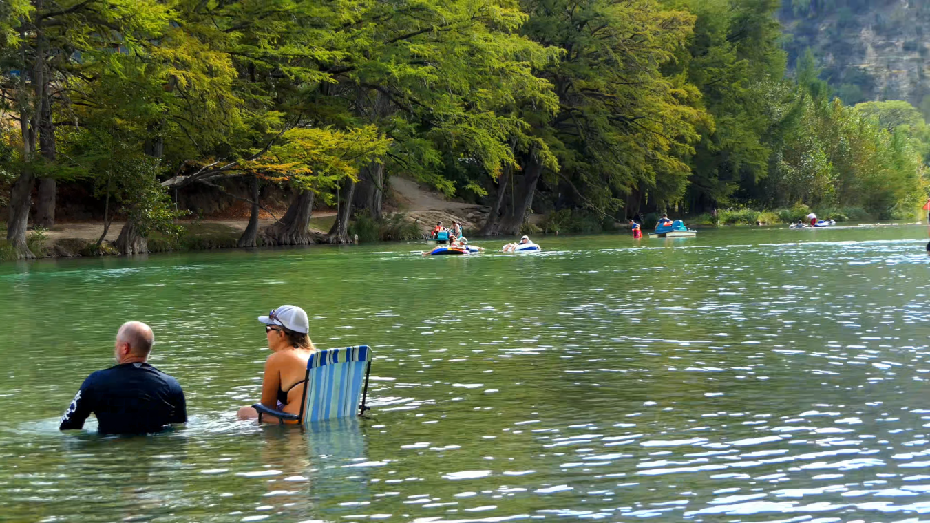 Young couple floating on raft, others enjoying a calm river in central Texas
