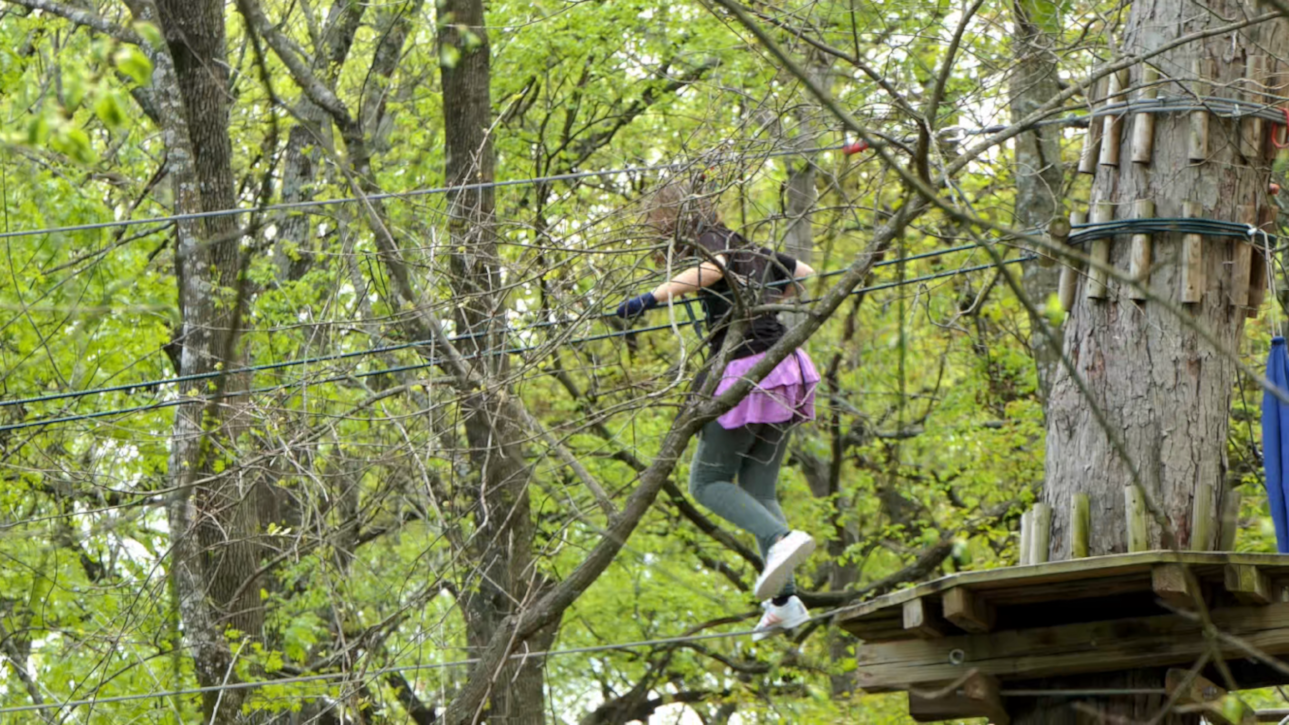 Teenage girl walks between trees on suspended cable at elevated obstacle course