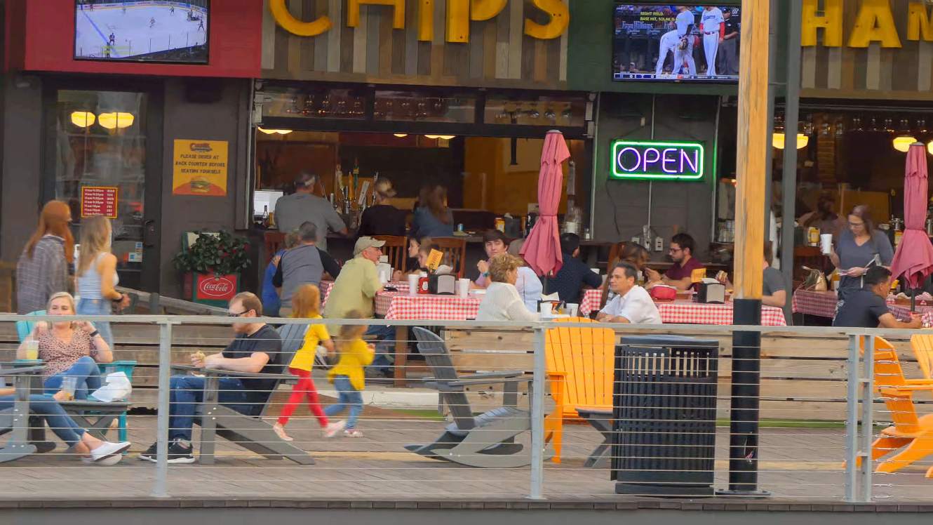 Zoom out from telephoto of open air bar and restaurant on boardwalk with pond