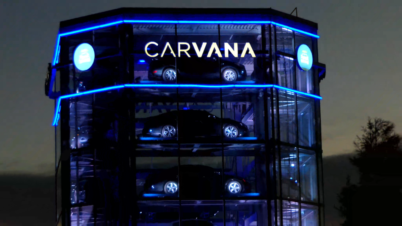 Zooming out from standalone Carvana car vending machine in blue lights at sunset