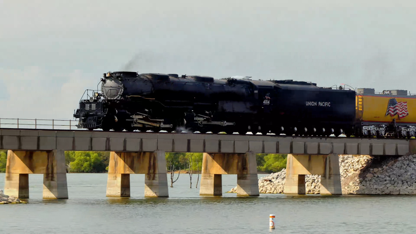 Big Boy 4014 steam locomotive emerges from trees to cross a short lake bridge