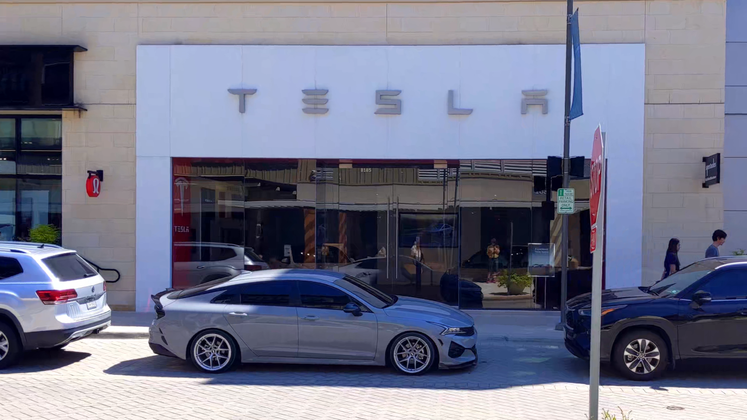 Walking across a street, filling the screen with the sign over TESLA dealership