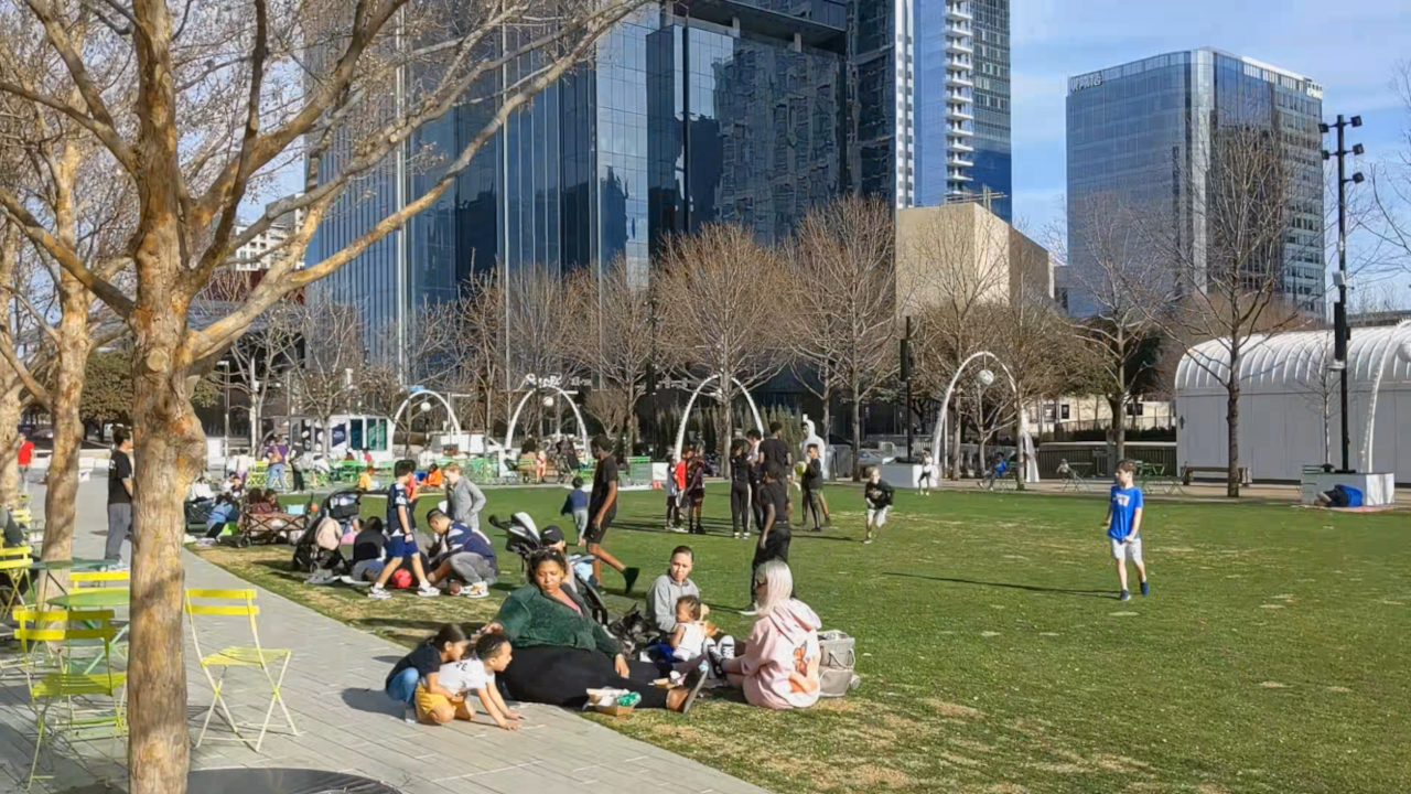 Children kicking balls on the grass in busy urban park, high-rise buildings